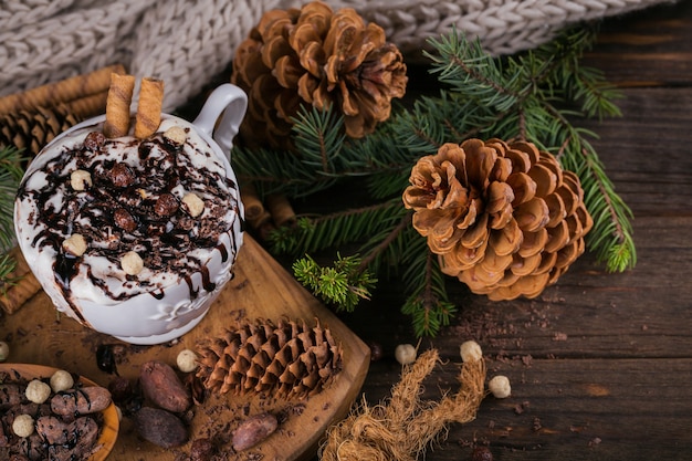 Composition de Noël ou du nouvel an avec une boisson au chocolat chaud ou au cacao avec de la crème fouettée servie avec du chocolat haché et des fèves de cacao sur une plaque en bois rustique.