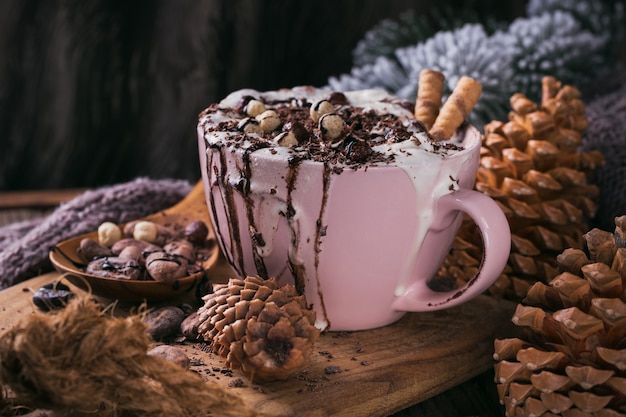 Composition de Noël ou du nouvel an avec une boisson au chocolat chaud ou au cacao avec de la crème fouettée servie avec du chocolat haché et des fèves de cacao sur une plaque en bois rustique.