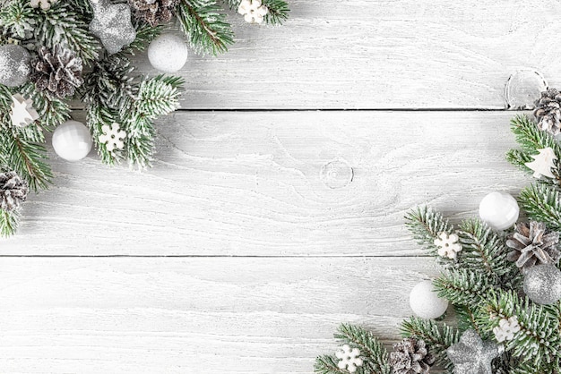 Composition de Noël faite de branches de sapin, décorations de vacances en argent sur fond de bois blanc.
