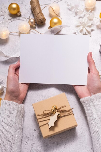 Composition de Noël, les mains féminines tiennent une carte postale vide. Décoration de Noël de couleur blanche.