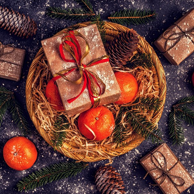 Composition de Noël avec des mandarines, des coffrets cadeaux, des cônes sur fond sombre.