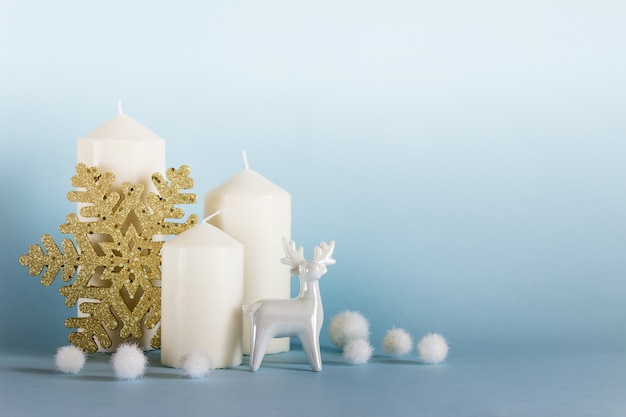 Composition de Noël, nouvel an avec trois bougies blanches, renne en porcelaine blanche, flocon de neige doré et boules blanches sur fond jaune bleu. Photo avec copie espace vide.