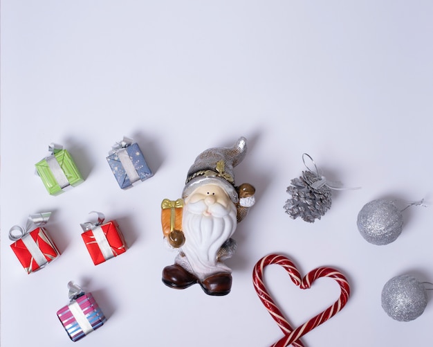 Composition de Noël avec le père Noël ou le gnome, cadeaux, cannes de Noël en forme de coeur, boules violettes et argentées, pommes de pin sur fond blanc, mise à plat, vue de dessus, espace pour copie