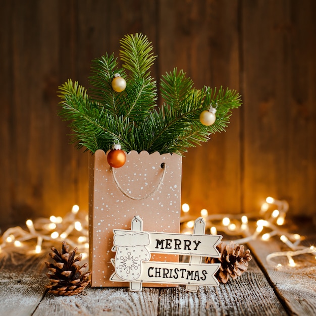 Composition de Noël. Sac en papier avec et bosses de branches de sapin sur fond en bois marron et lumières bokeh.