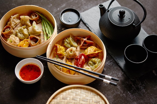 Composition de la nourriture chinoise Variétés mixtes de boulettes à la vapeur en bambou servies avec du soja et des sauces épicées et du thé traditionnel dans une casserole en fer