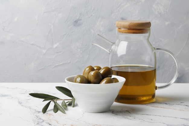 Composition d'olives vertes à l'huile, rameau d'olivier, saucière sur fond de marbre. Espace pour le texte.