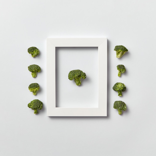 Composition organique créative avec du brocoli vert fraîchement cueilli dans un cadre et hors de celui-ci sur un mur gris clair, place pour le texte. Mise à plat. Concept végétalien.