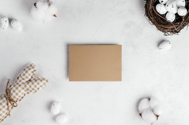 Composition De Pâques De Carte Postale Beige Vierge Beige Vide Sur Fond De Papier Gris Blanc Et Oeufs De Caille à Petites Taches Blanches Dans Un Nid Naturel Brun Oiseau Près De Fleurs De Coton Lapin Jouet Fête Traditionnelle