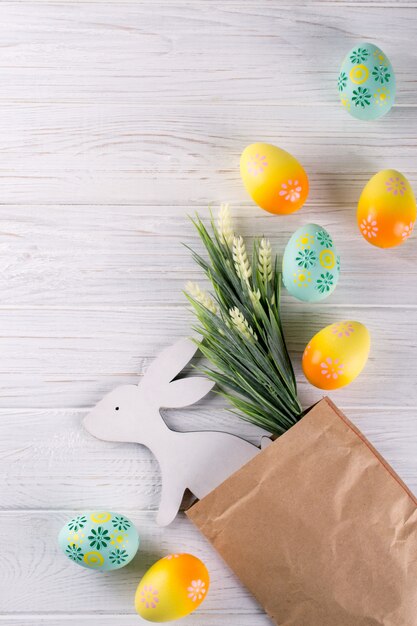 Composition de Pâques avec emballage en papier artisanal, oeufs de Pâques colorés, lapin en bois décoratif et fleurs. Mise à plat, vue de dessus, espace copie