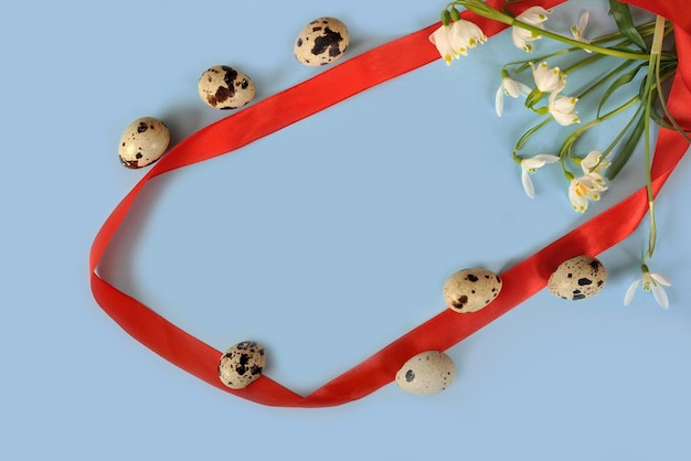 Composition de Pâques avec des fleurs de perce-neige, des œufs de caille et un ruban rouge sur fond bleu