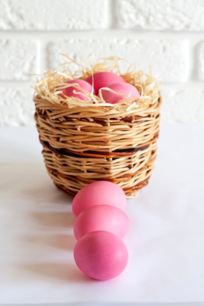 Composition de Pâques minimaliste avec panier en osier et oeufs de couleur rose sur fond blanc