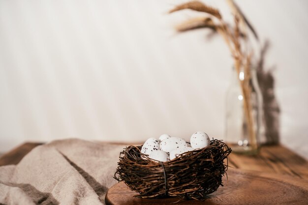 Composition de Pâques d'oeufs de caille dans un nid sur une table en bois et une branche de blé en verre sur fond flou blanc beige Célébration d'un événement traditionnel fête vacances Style de confort rustique