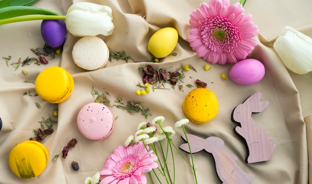 Composition de Pâques avec des oeufs multicolores, des figurines de lapins, des fleurs fraîches et des gâteaux de macarons