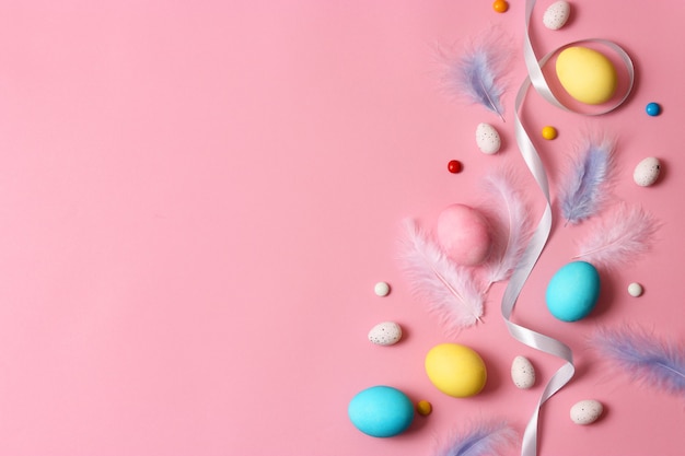 Composition de Pâques des oeufs et des plumes peints sur un fond coloré