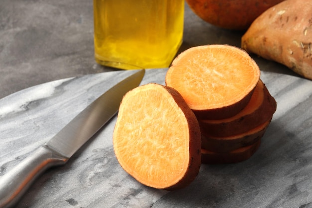 Composition de patates douces fraîches, de beurre et de couteau en tranches sur un gros plan de fond de marbre.