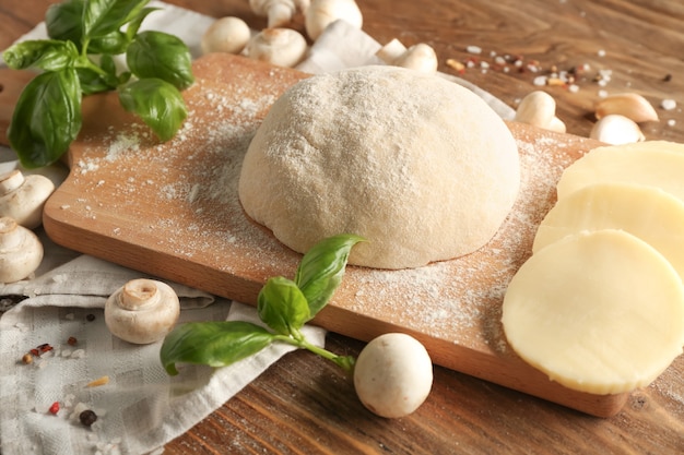 Composition avec pâte crue et ingrédients pour pizza sur table en bois