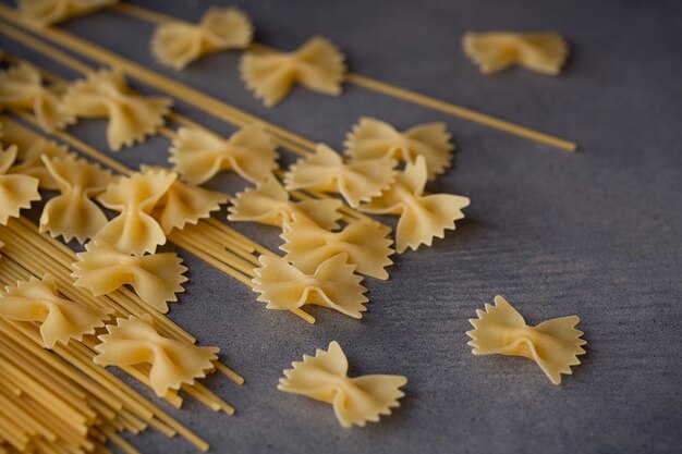 Composition de pâtes italiennes non cuites. Spaghetti, farfalle, fusilli sur fond de bois foncé. Fond de pâtes crues.