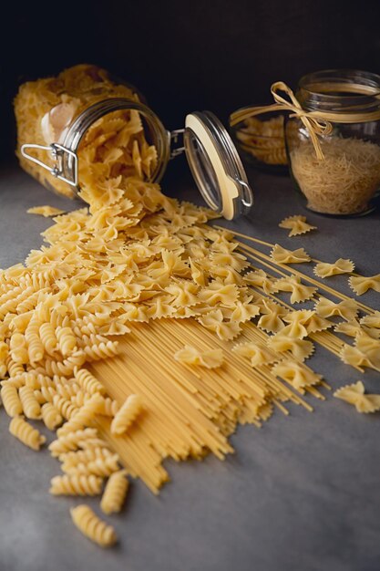 Composition de pâtes italiennes non cuites. Spaghetti, farfalle, fusilli sur fond de bois foncé. Fond de pâtes crues.