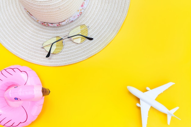 Composition de plage d'été. Mise à plat simple minimale avec chapeau de lunettes de soleil d'avion et flamant gonflable isolé sur fond jaune. Concept de voyage aventure voyage vacances. Espace de copie vue de dessus.