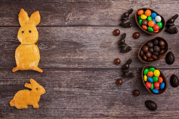 Composition à plat avec oeufs de Pâques au chocolat, lapin et bonbons sur fond en bois foncé. Vue de dessus. Avec copie espace