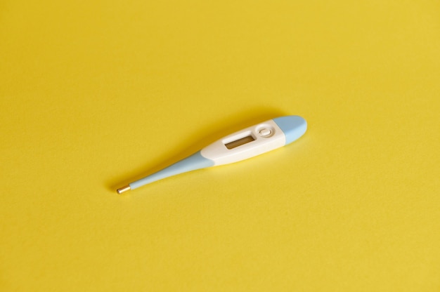 Composition à plat d'un thermomètre numérique sur fond jaune avec espace de copie. Prise de vue en studio avec une ombre douce