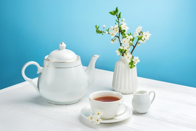 Composition printanière avec une théière, une tasse de thé et une branche de cerisier en fleurs sur fond bleu