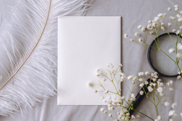 Composition de printemps, papier blanc vide, fleurs de gypsophile, loupe et plume blanche