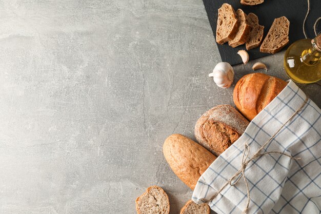 Composition avec des produits de boulangerie, de l'ail, de l'huile d'olive et du torchon sur un espace gris, vue de dessus et espace pour le texte