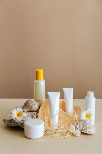 Composition de produits cosmétiques de beauté pour les soins de la peau avec coquillage sur fond beige piédestal en pierre. Maquette de tube de bouteille cosmétique crème naturelle avec des fleurs tropicales.