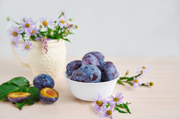 La composition de prunes et de fleurs sauvages sur une surface en bois clair.