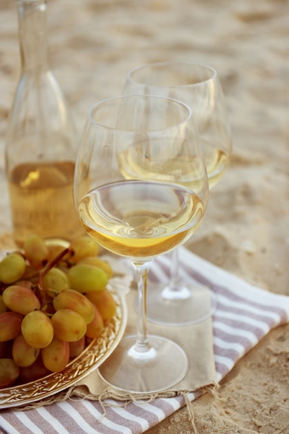 Composition romantique de vin blanc et de raisin sur une plage de sable