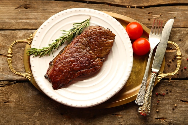 Composition avec savoureuse viande rôtie sur assiette tomates et brins de romarin sur fond bois