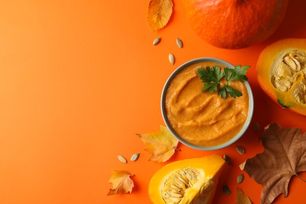 Composition avec soupe de potiron, graines et feuilles sur orange