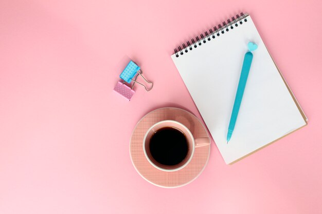 Composition de tasse de café, cahier, stylo sur fond rose