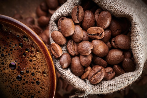 Composition d'une tasse de café fraîchement infusée et de grains de café torréfiés dans un sac sur fond marron