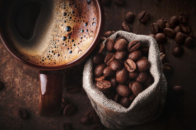 Composition d'une tasse de café fraîchement infusée et de grains de café torréfiés dans un sac sur fond marron