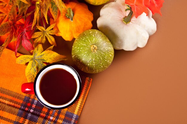 Composition avec une tasse rouge avec du thé, des feuilles d'automne et de petites citrouilles sur le fond des muscles. Récolte d'automne. Notion d'automne.