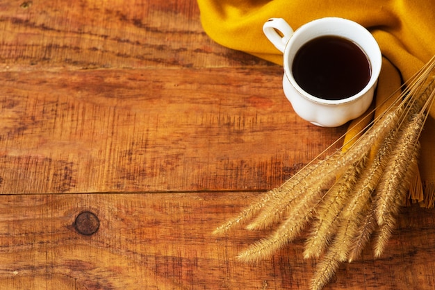 Composition de tasse de thé d'automne, écharpes jaunes et épillets de blé sur fond de bois