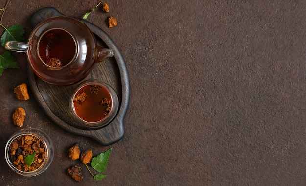 Composition de thé chaga, morceaux de champignons chaga, feuilles de bouleau vert sur fond marron. Boisson saine à la mode. Copiez l'espace, vue de dessus, pose à plat.