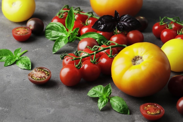 Composition de tomates fraîches mûres de différentes variétés, mini poivrons, épices, rammarine, thym, basilic, piment, sur un fond texturé en béton avec un espace pour le texte.