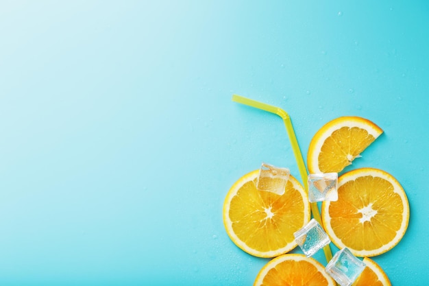 Une composition de tranches d'orange et de glaçons avec une paille sur fond bleu sous forme de boisson rafraîchissante. Vue de dessus, espace libre