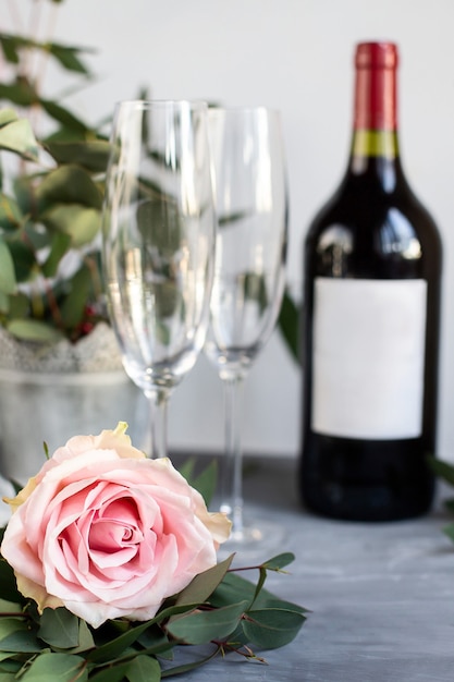 Composition avec verre, fleurs et bouteille de vigne sur fond de béton gris.