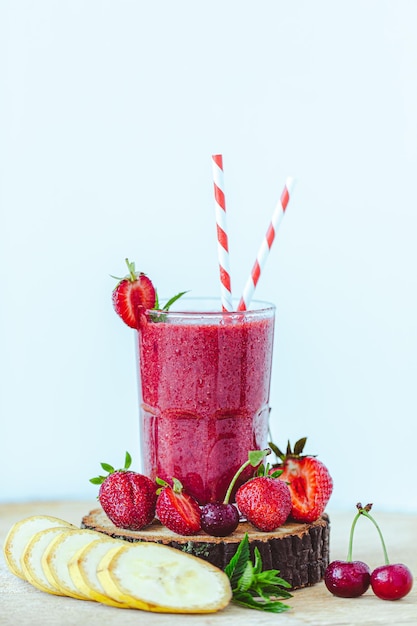 Composition de verre avec smoothie cramoisi frais avec banane et baies sur fond bleu