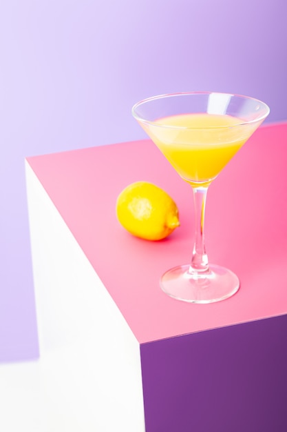 Composition vive et lumineuse avec verre à cocktail de boisson jaune et citron frais placé sur fond coloré