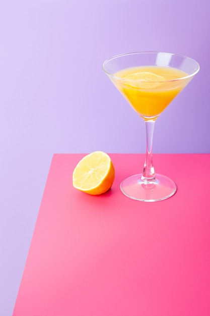 Composition vive et lumineuse avec verre à cocktail de boisson jaune et citron frais placé sur fond coloré