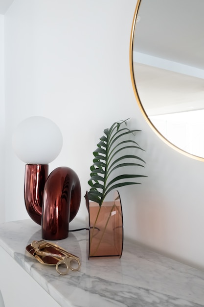 Composition de vue verticale élégante de lampe de table miroir rouge avec stationnaire d'or sur le dessus en marbre blanc avec copie espace sur mur blanc