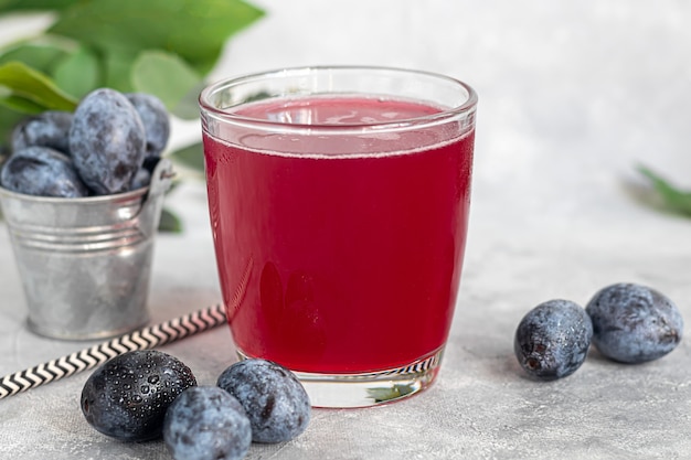 Compote de prunes dans un verre. En arrière-plan, il y a des prunes. Sauce tkemali. Se préparer pour l'hiver. Fond clair.