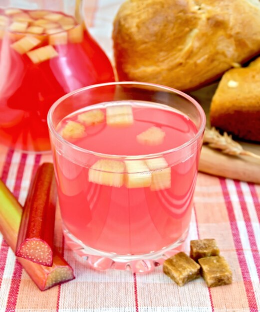 Compote de rhubarbe dans un verre et un pichet, tiges de rhubarbe, sucre, pain sur fond de nappe