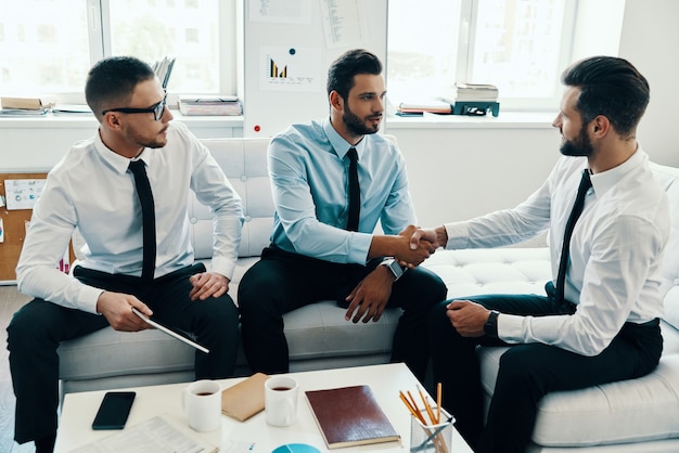 Compréhension mutuelle. Jeunes hommes modernes en tenues de soirée se serrant la main tout en travaillant au bureau