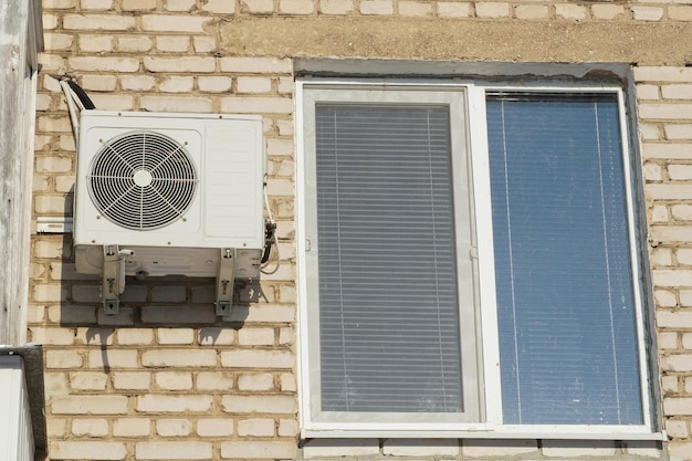 Photo le compresseur du climatiseur accroché au mur d'un immeuble résidentiel à côté de la fenêtre